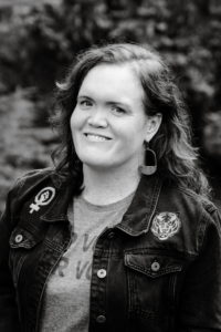 portrait of carrie. woman with wavy shoulder length hair wearing black jacket with tiger and woman's empowerment symbol